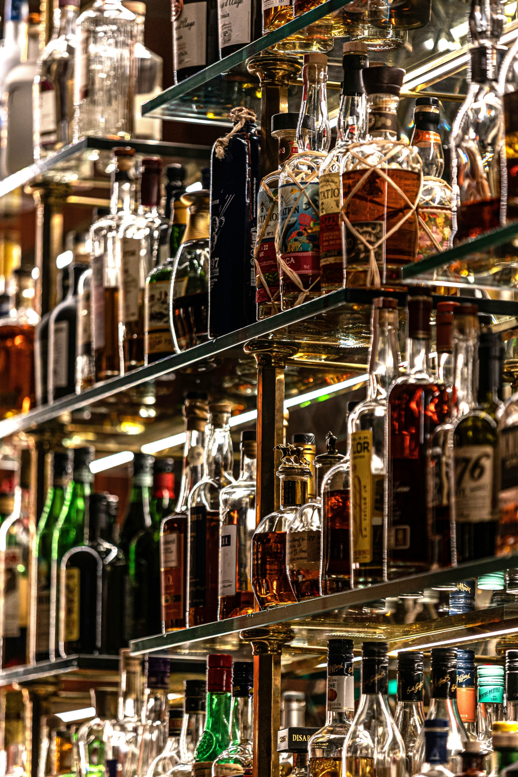 Bottles of distilled spirits and liqueurs on glass shelves in a bar